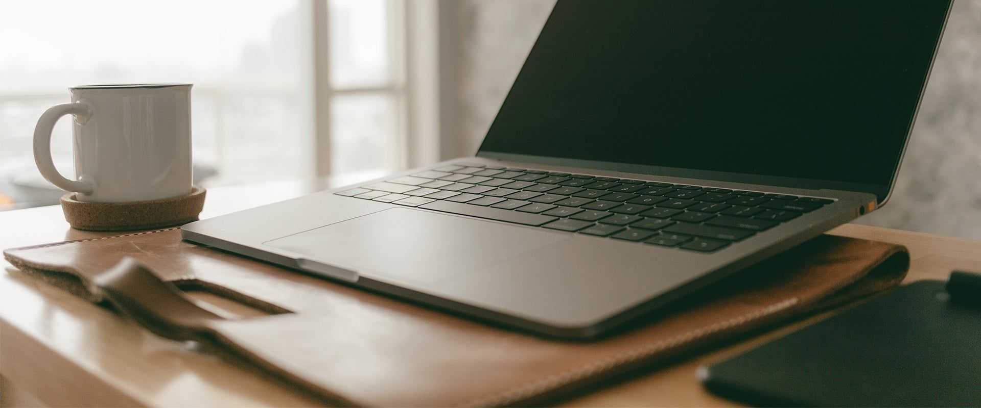 Laptop on a computer desk with a coffee cup besides it.